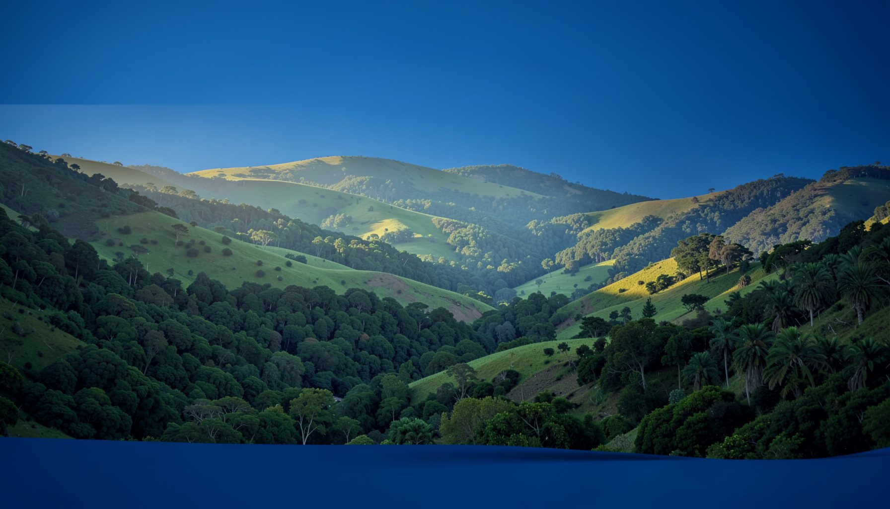 Soft morning light rolling over the green hills and valley of Otxandio, with muted blue and forest-green tones in a wide landscape photograph